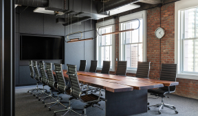 A modern conference room featuring black walls and a wooden table, designed for professional meetings in an office setting.