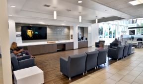 A lobby in an office with people sitting in chairs and a television.