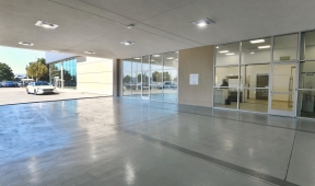 Empty office parking lot with large windows and a car in the background.