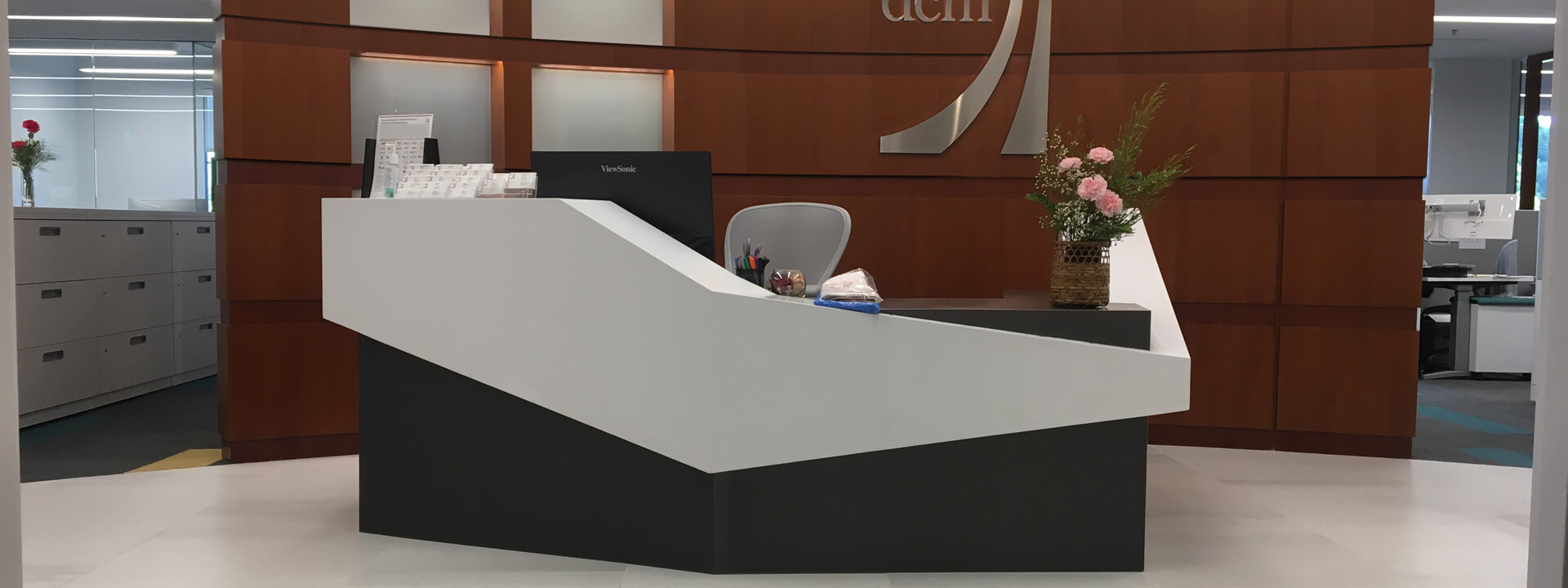 Reception desk in office with large wall, modern design, computer monitor, potted plant, chairs