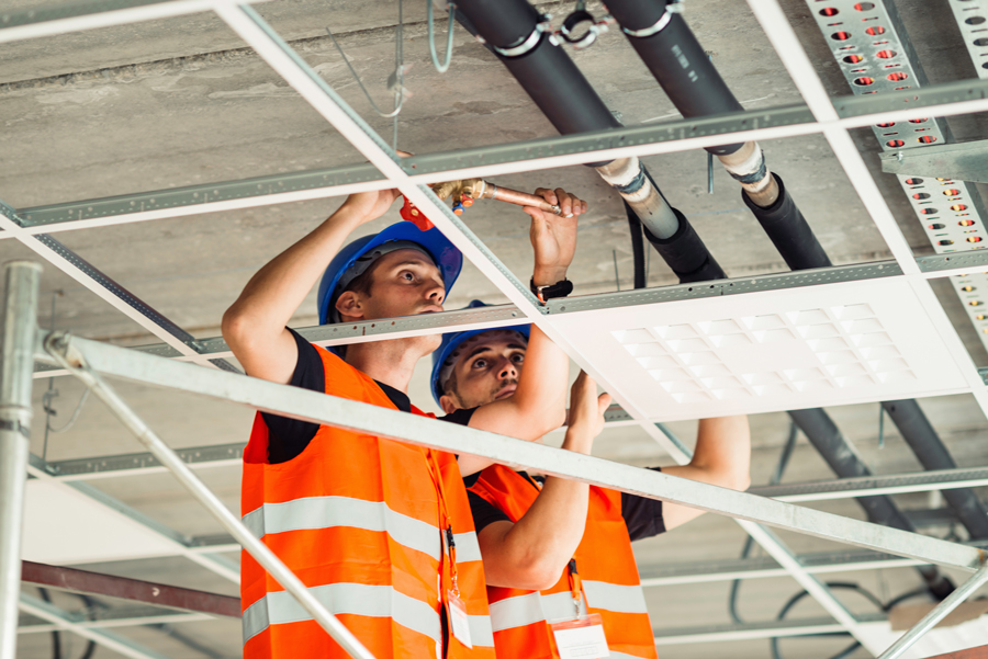 Construction workers in orange vests repairing a ceiling indoors.