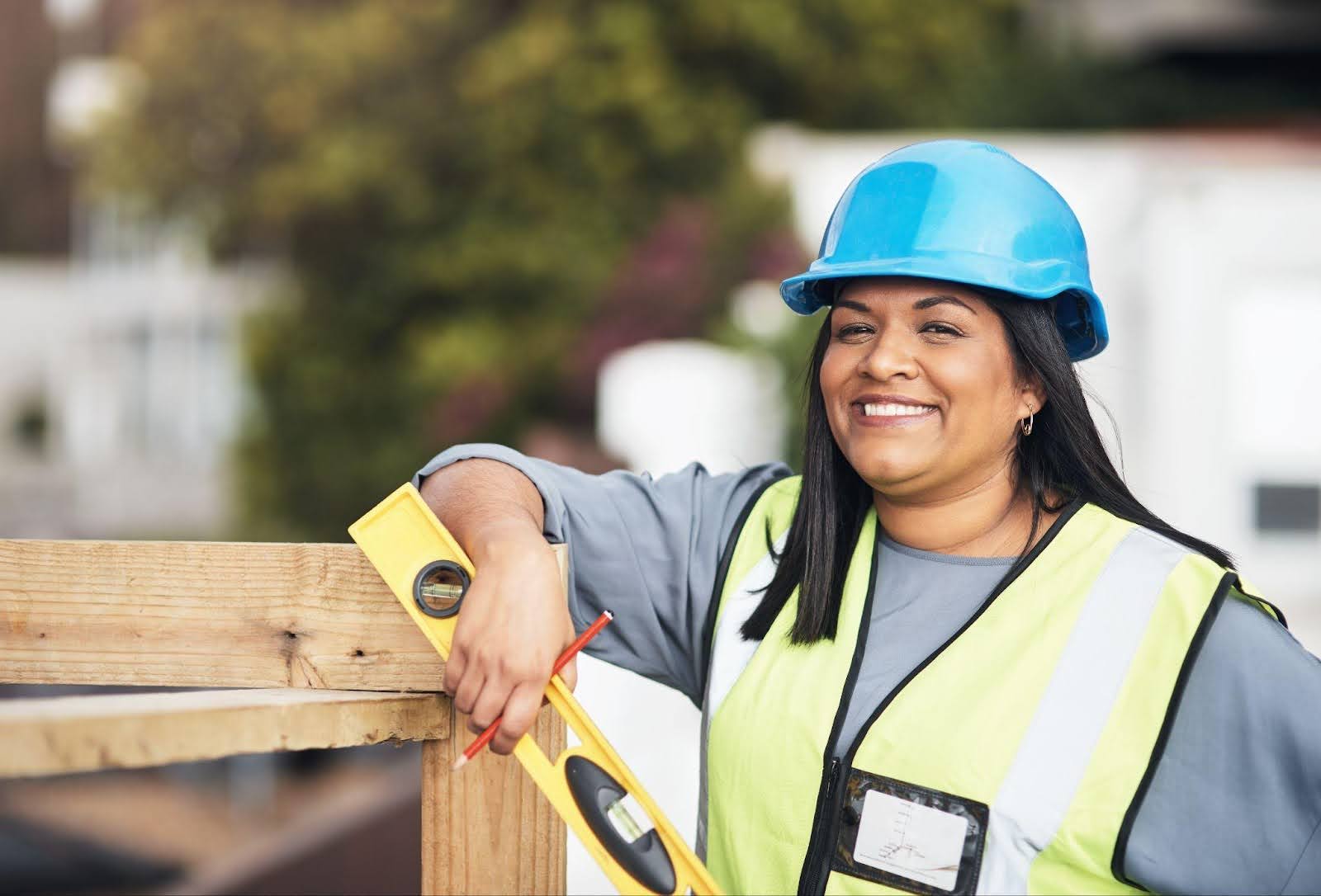 A woman in a hard hat and safety vest uses a measuring tape, illustrating her role in construction safety