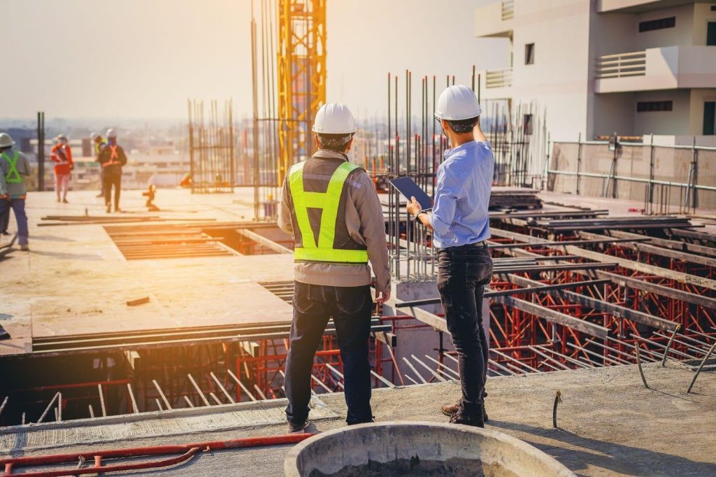 Two workers in safety gear are on a site with scaffolding and tools