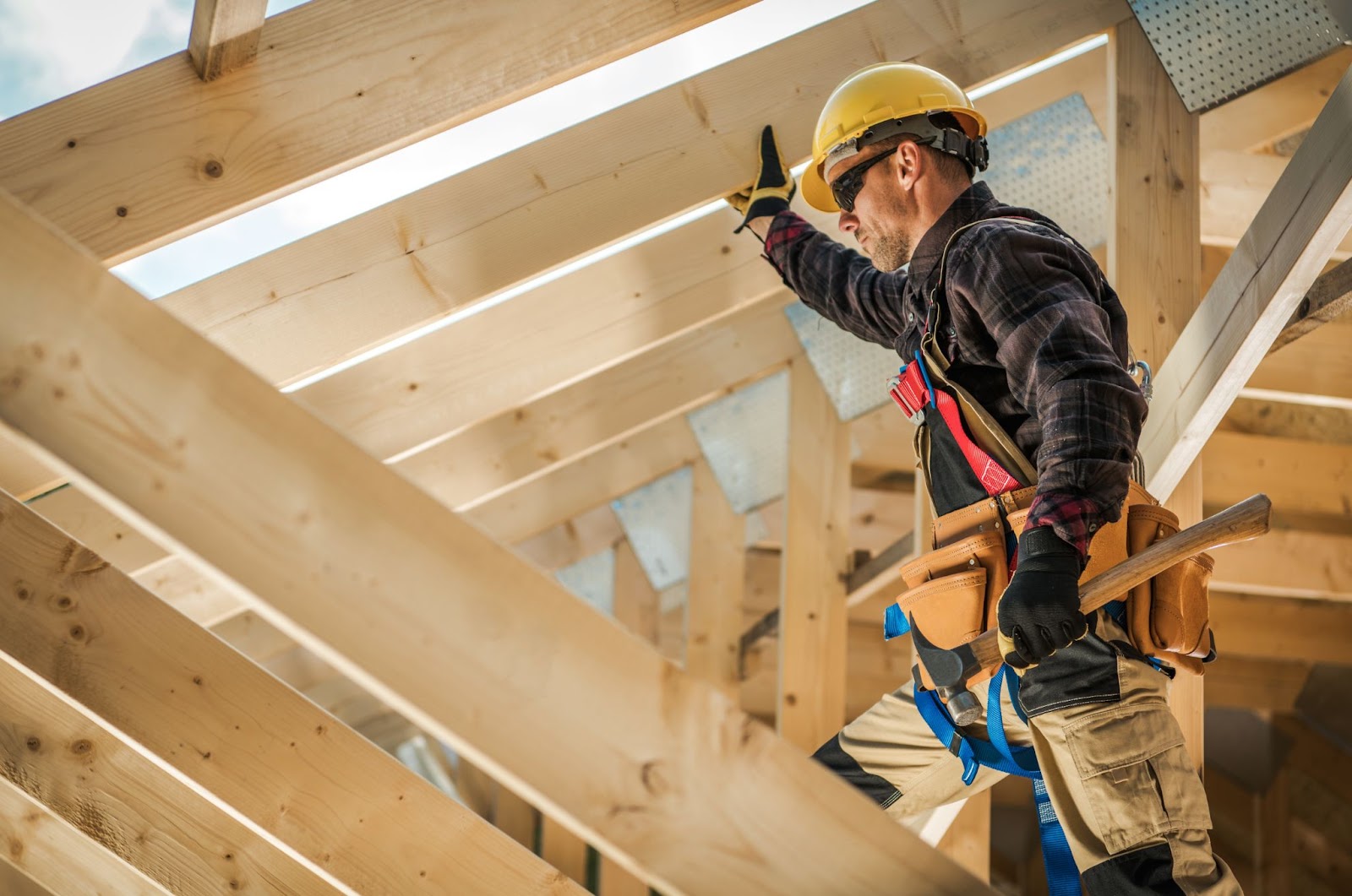 A commercial construction contractor in a hard hat and safety vest working diligently on a roof.