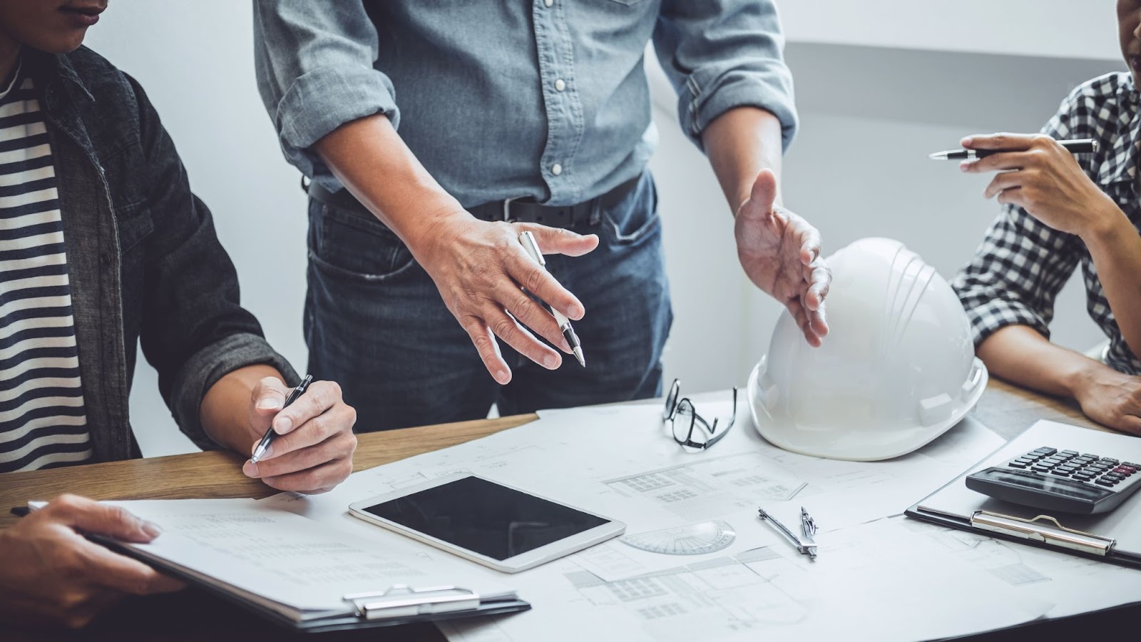 A group of professionals at a table, discussing plans, with a hard hat symbolizing their work in commercial construction.