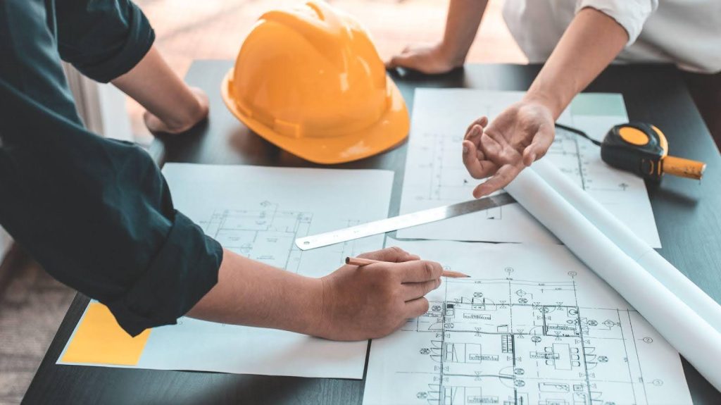 Two professionals in hard hats reviewing construction plans together