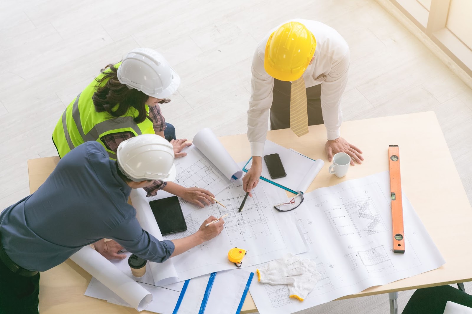 Three individuals in hard hats and safety vests collaborating on construction plans, demonstrating their experience in commercial projects.