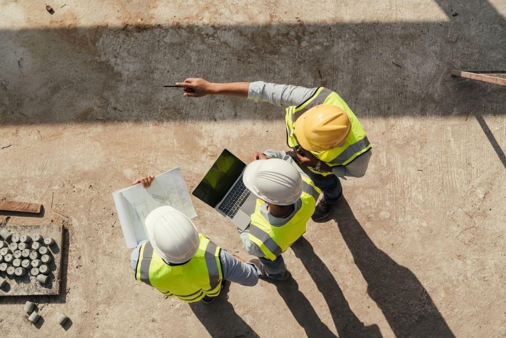 Three construction workers in hard hats and safety vests collaborating on-site